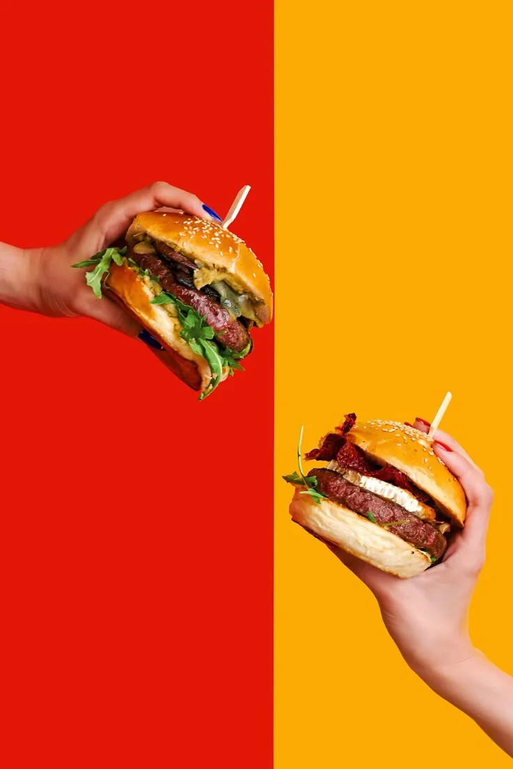 Two burgers held against red and yellow backgrounds